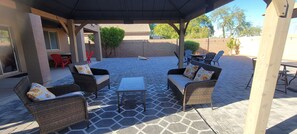 An outdoor patio with wicker furniture, a glass table, and a brick floor. - Charming 4 bed / 3 bath house, full amenities! (Sun City)