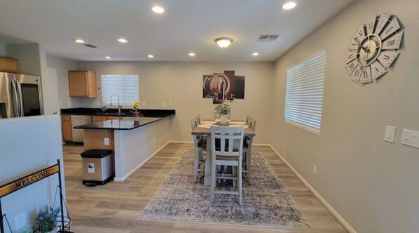 A modern kitchen with a dining area, wooden cabinets, a clock, and a welcome sign.