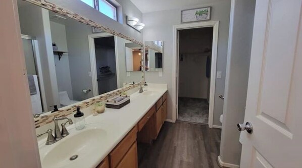 A bathroom with a large mirror, a sink, and a shower area. - Charming 4 bed / 3 bath house, full amenities! (Sun City)
