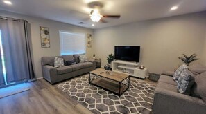 A living room with a grey sofa, a coffee table, a TV, and a ceiling fan.