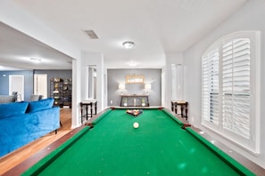 Une table de billard recouverte d’un drap vert, entourée de murs blancs et d’un canapé bleu.