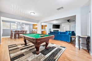 Un salon spacieux avec une table de billard, un canapé bleu et un téléviseur.