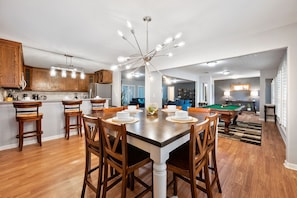 Une cuisine moderne avec des meubles en bois, un coin repas doté d’une grande table et de chaises, et une table de billard à l’arrière-plan.