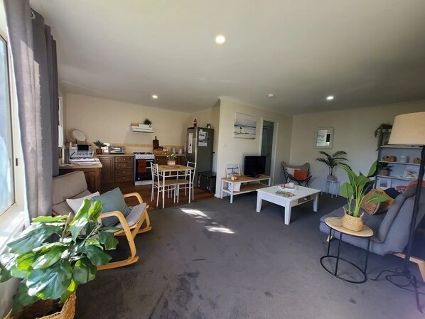 A compact living space with a kitchenette, a dining area, a seating area with a sofa and armchairs, and a television.