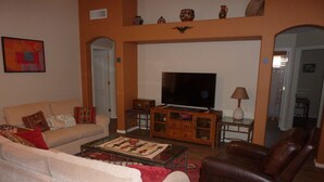 A living room with a sofa, a brown leather chair, a television, and a cabinet with decorative items.