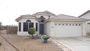 A single-story house with a tiled roof, a garage, and a small front yard with a potted plant and a birdbath.