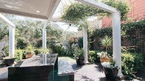 A covered patio area with a wooden deck, white columns, and potted plants. - Banksia by the Bay (Collingwood Park)