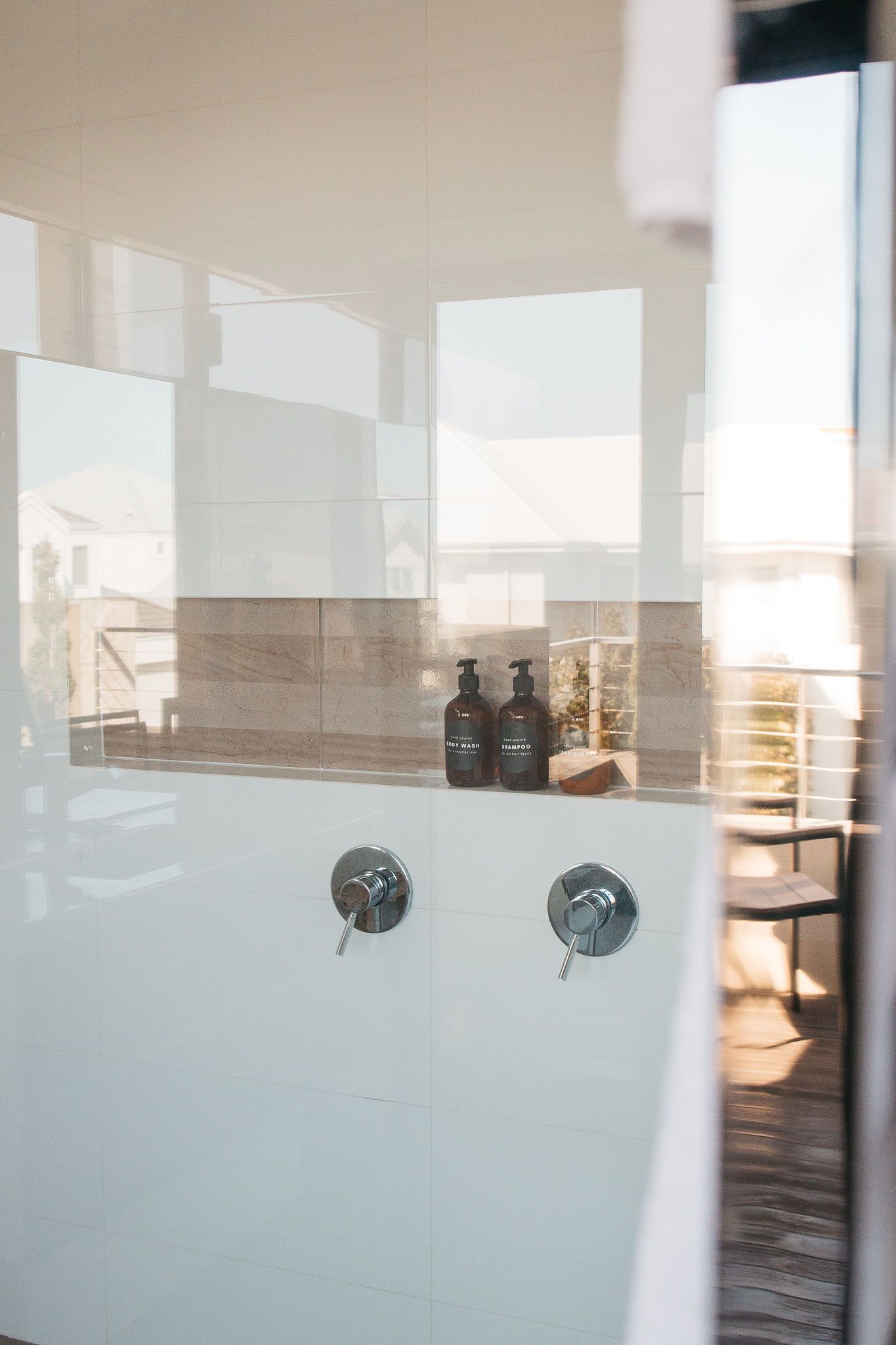 Une salle de bain moderne avec une douche à l’italienne en verre, un pare-baignoire en marbre et deux bouteilles de shampoing.