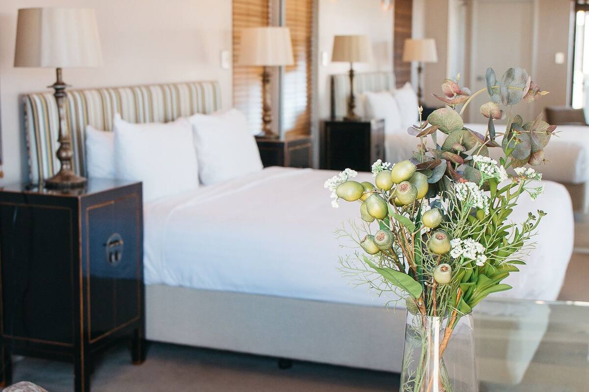 A hotel room with a bed, bedside tables, a glass coffee table, and a vase with flowers.