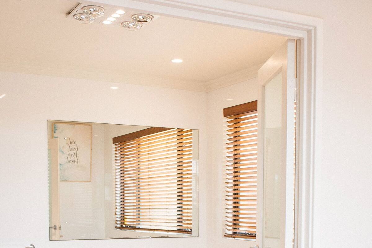 A bedroom with a large bed, a white bathroom with a double sink, and a mirror above the sink.