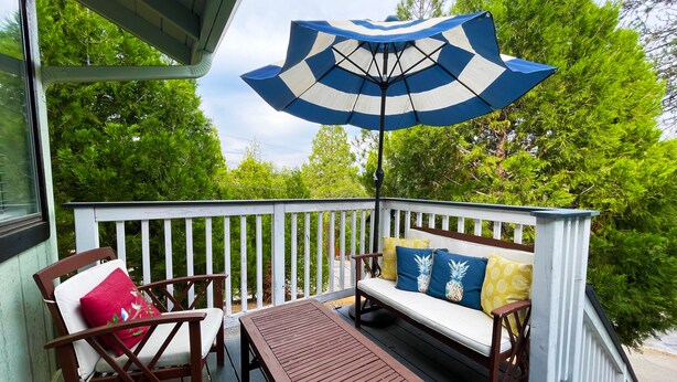 A wooden deck with a white railing, a brown table, and a blue and white striped umbrella. - Recharge Retreat and Spa Near Yosemite (Groveland)