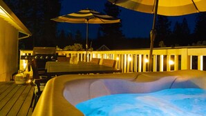 A hot tub with a wooden deck and outdoor furniture, surrounded by a wooden deck with lights. - Recharge Retreat and Spa Near Yosemite (Groveland)