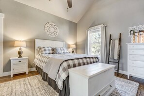 A bedroom with a bed, two bedside tables, a dresser, a window with curtains, a decorative wall piece, and a wooden ladder.
