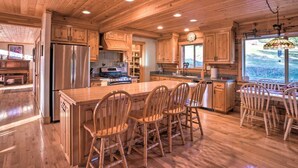 Una cocina amplia con armarios de madera, una isla grande con taburetes de bar, un refrigerador de acero inoxidable y vistas al exterior a través de una ventana.
