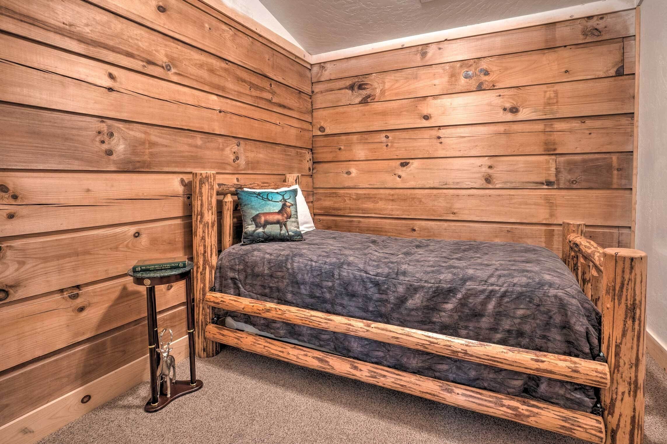 A wooden bunk bed with a dark blanket, a pillow with a deer design, and a small wooden nightstand with a book and a decorative item.