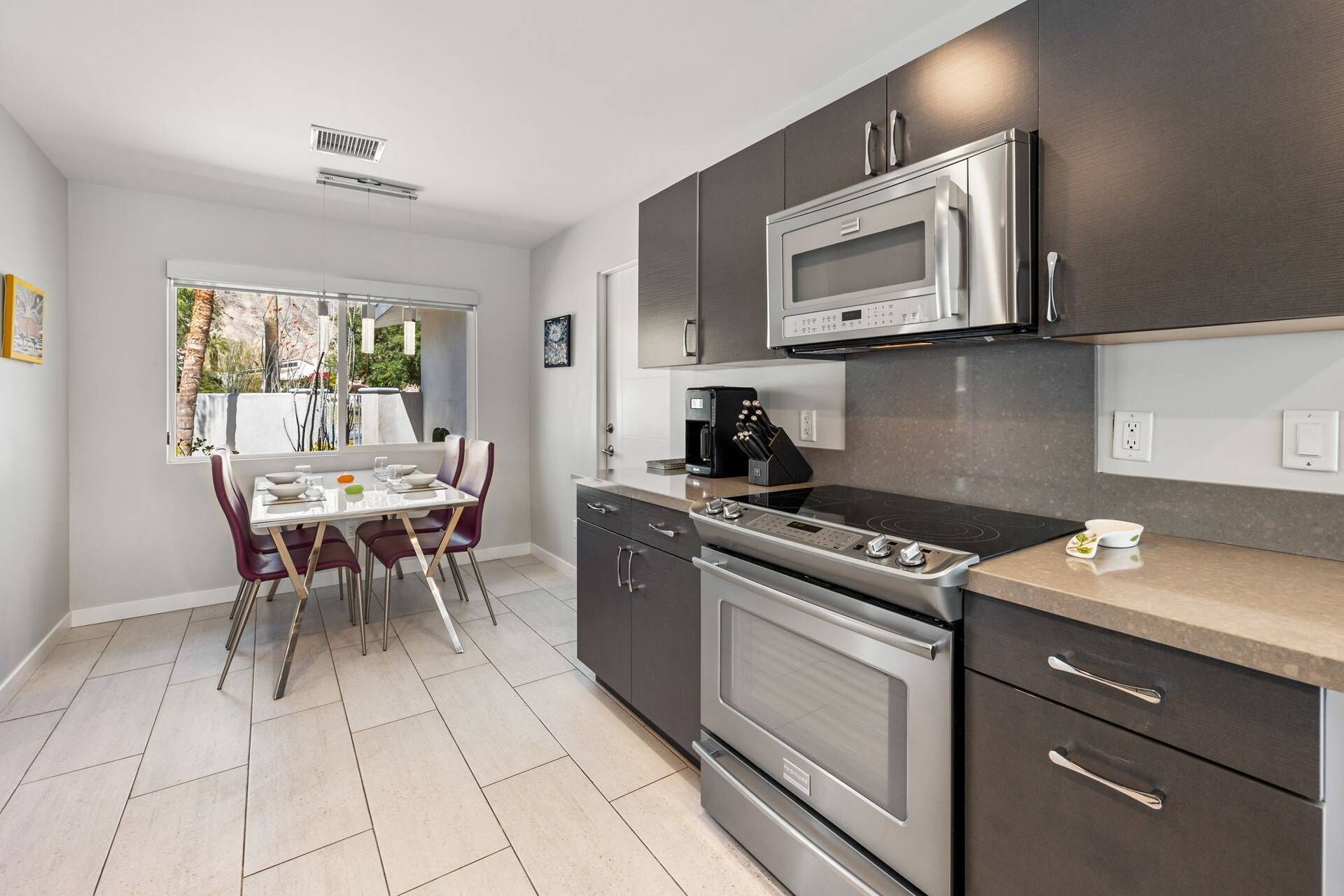 Una cocina moderna con muebles oscuros, electrodomésticos de acero inoxidable y un comedor con mesa y sillas.