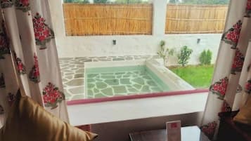 A room with a glass table, a sofa, and a view of a courtyard with a wooden fence and greenery.