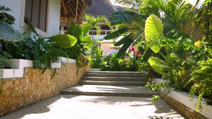 A stone staircase surrounded by lush tropical plants leading to a building with a thatched roof. - The Diamond of Africa - Luxury Villa (Malindi)