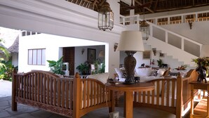 A spacious lounge area with a wooden bench, a table with a lamp, and a staircase leading to an upper level. - The Diamond of Africa - Luxury Villa (Malindi)