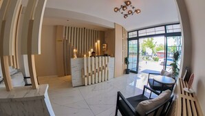 A modern hotel lobby with a reception desk, seating area, and large windows offering a view of the street. - MOF Comfort Edirne (Edirne)