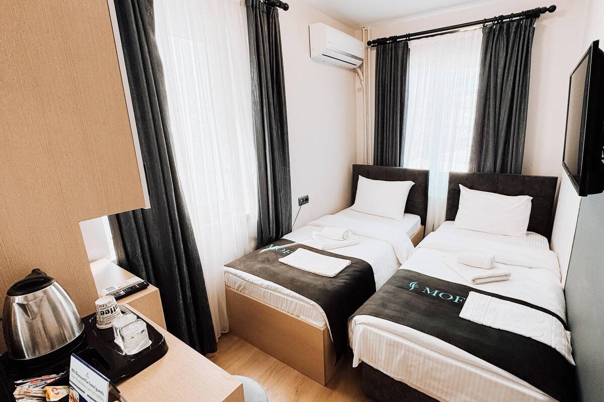 Ein Hotelzimmer mit zwei Betten, einem Schreibtisch mit Wasserkocher, einer Kaffeemaschine und einem an der Wand befestigten Fernseher.