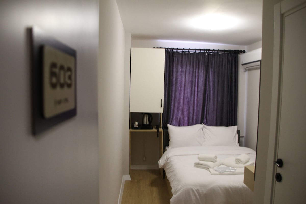 A hotel room with a bed, a nightstand, a mirror, and a door.