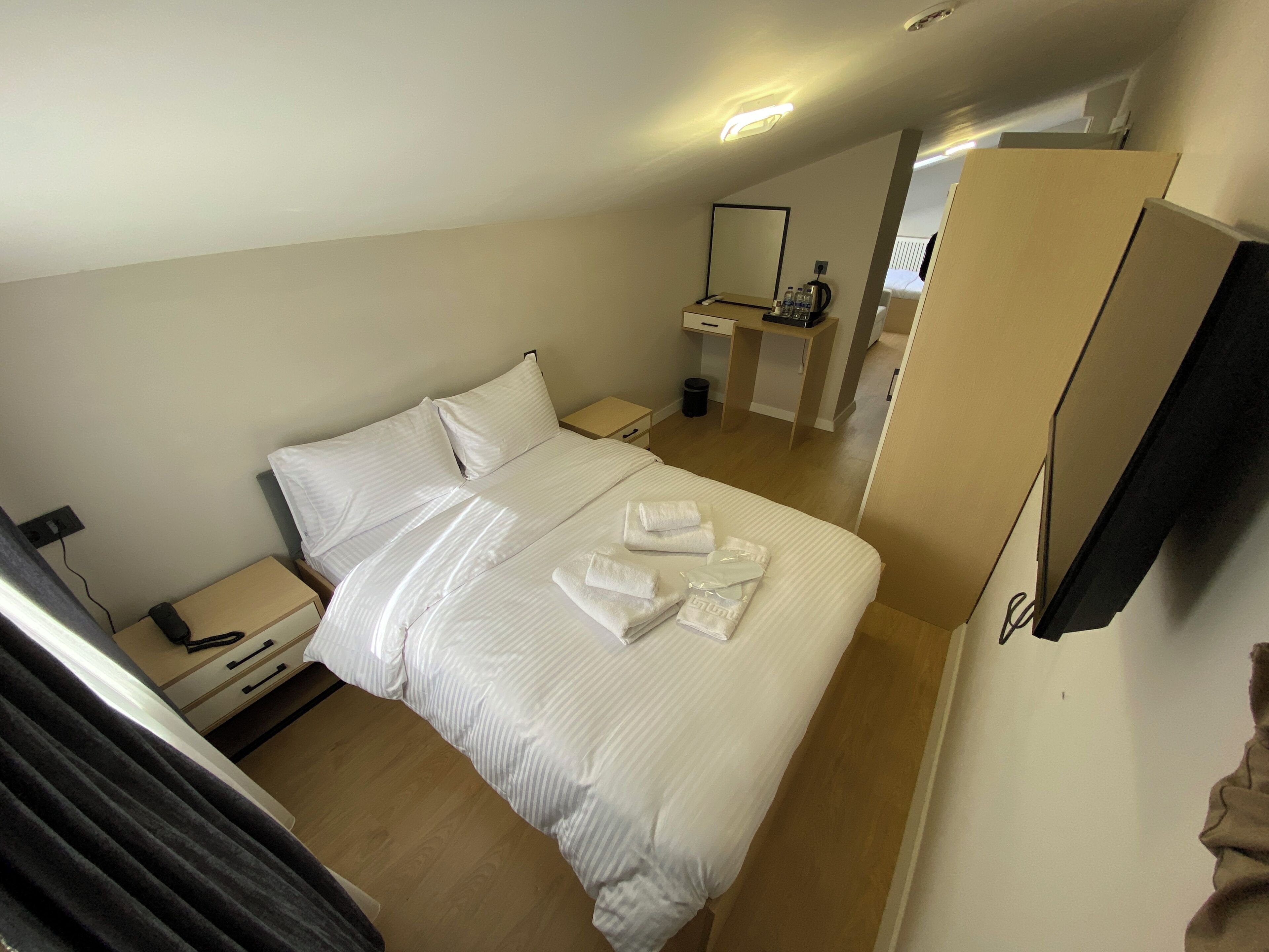 Habitación de hotel con cama, mesitas de noche, un espejo y un baño visible al fondo.