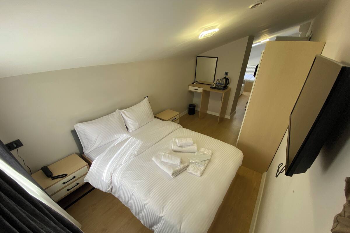 Ein Hotelzimmer mit einem Bett, Nachttischen, einem Spiegel und einem im Hintergrund sichtbaren Badezimmer.