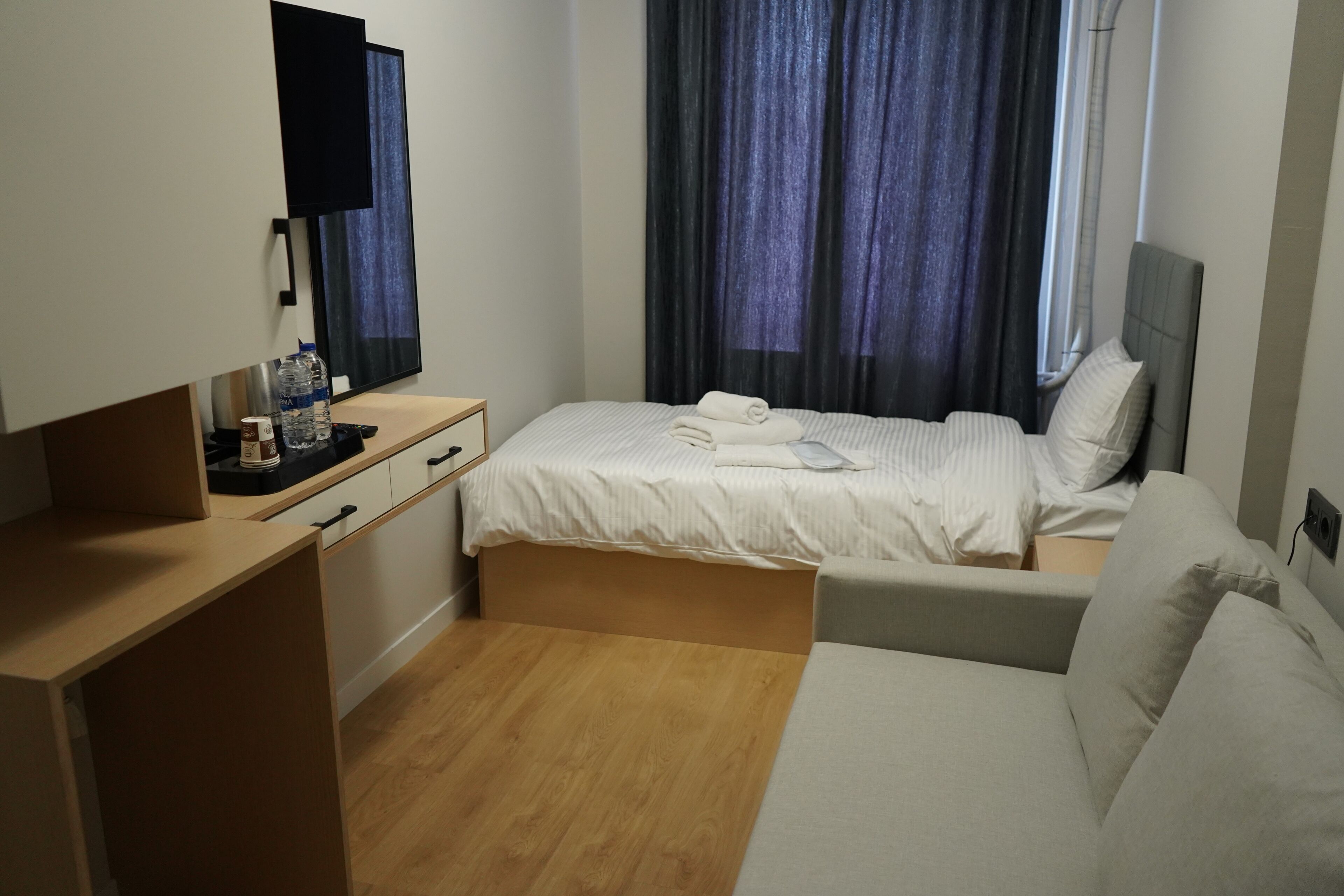 Ein Hotelzimmer mit Bett, Sofa, Schreibtisch, Spiegel und einem fenster mit Vorhängen.
