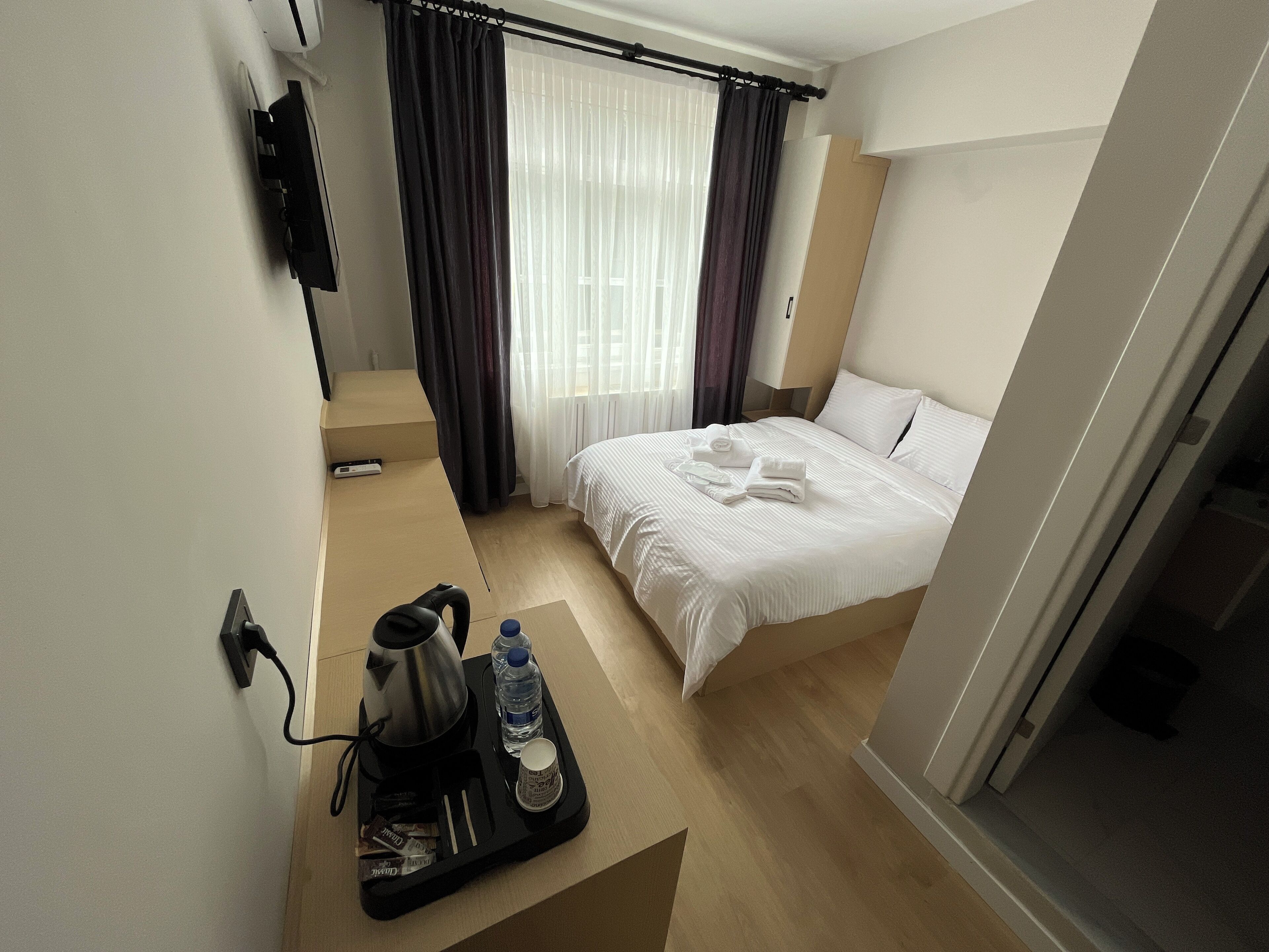 Habitación de hotel con cama, cafetera, botella de agua y bandeja con toallas.
