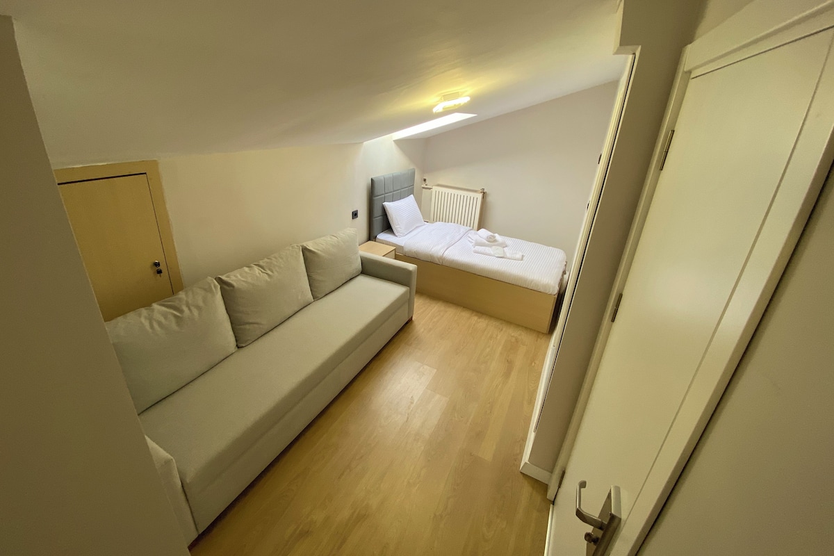 A small, compact room with a sofa, a bed, and a radiator.