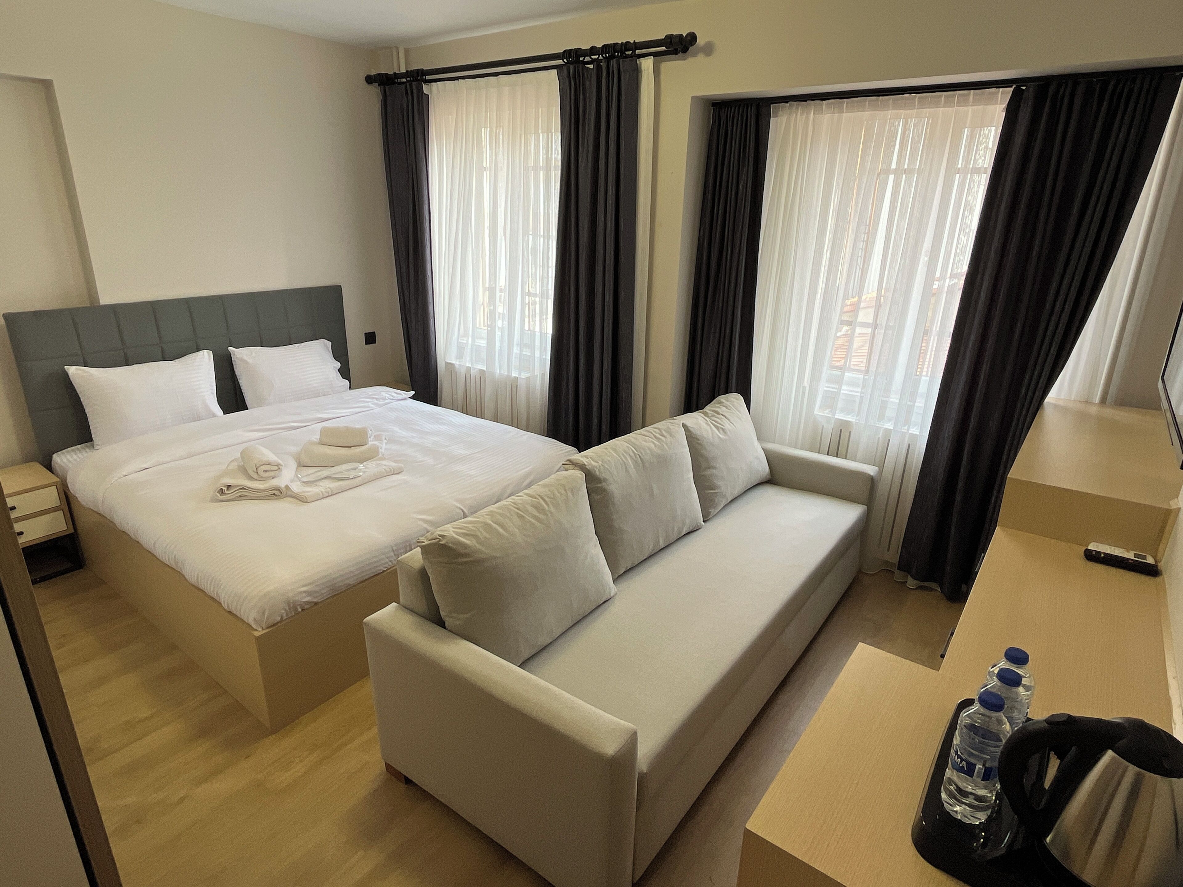 Una habitación de hotel con cama, sofá, mesita de noche, hervidor de agua y botella de agua.