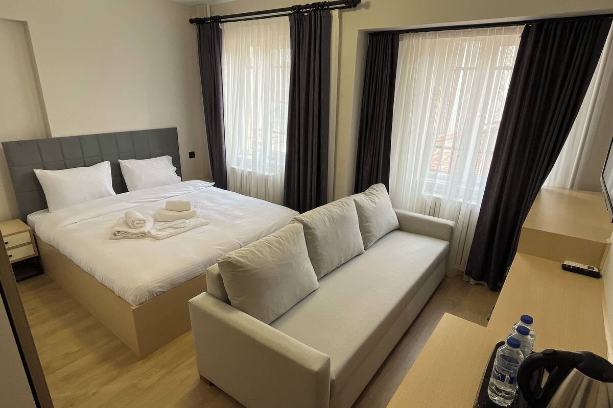 Ein Hotelzimmer mit einem Bett, einem Sofa, einem Nachttisch, einem Wasserkocher und einer Wasserflasche.