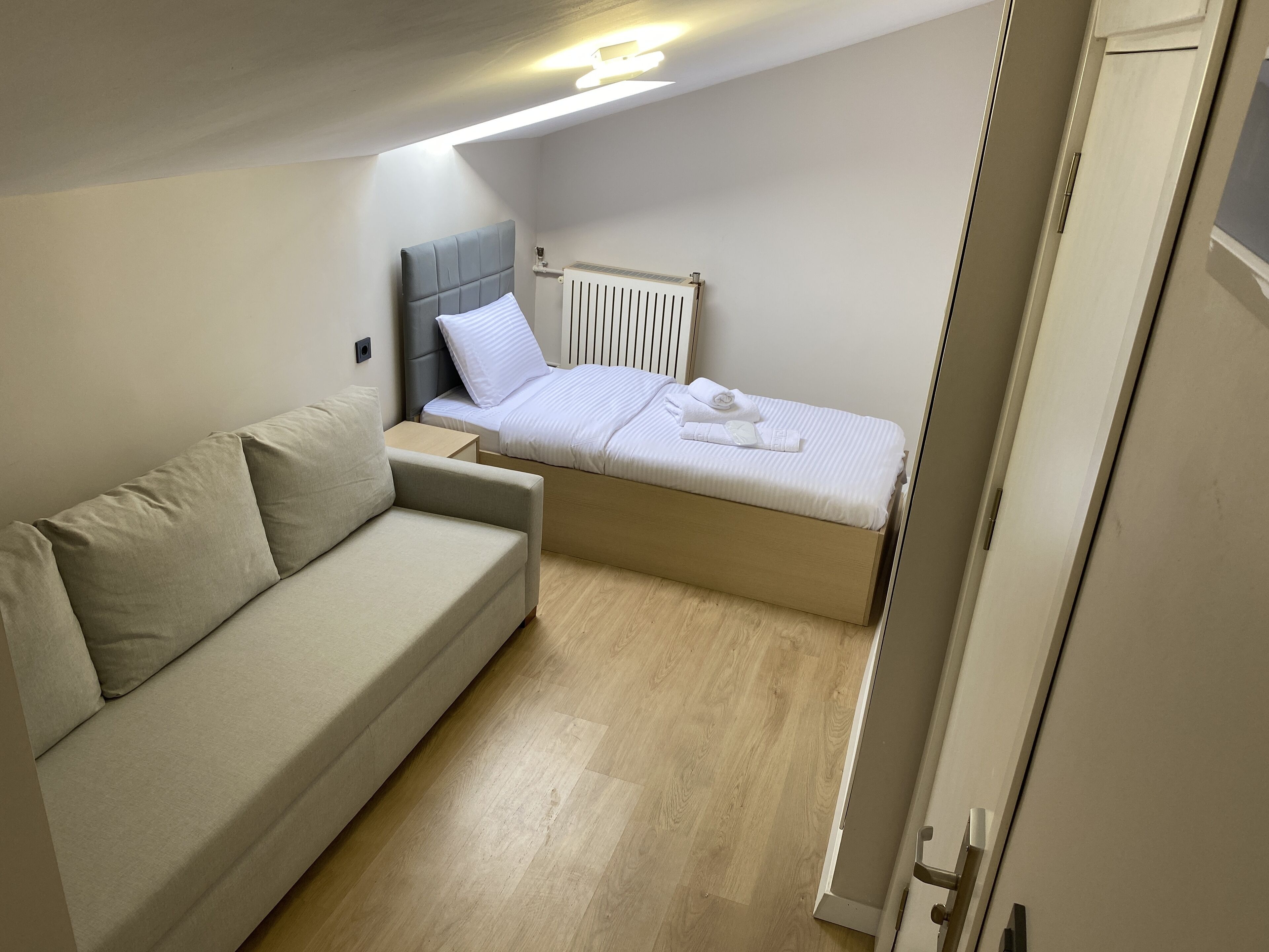 A compact bedroom with a bed, a sofa, and a radiator.