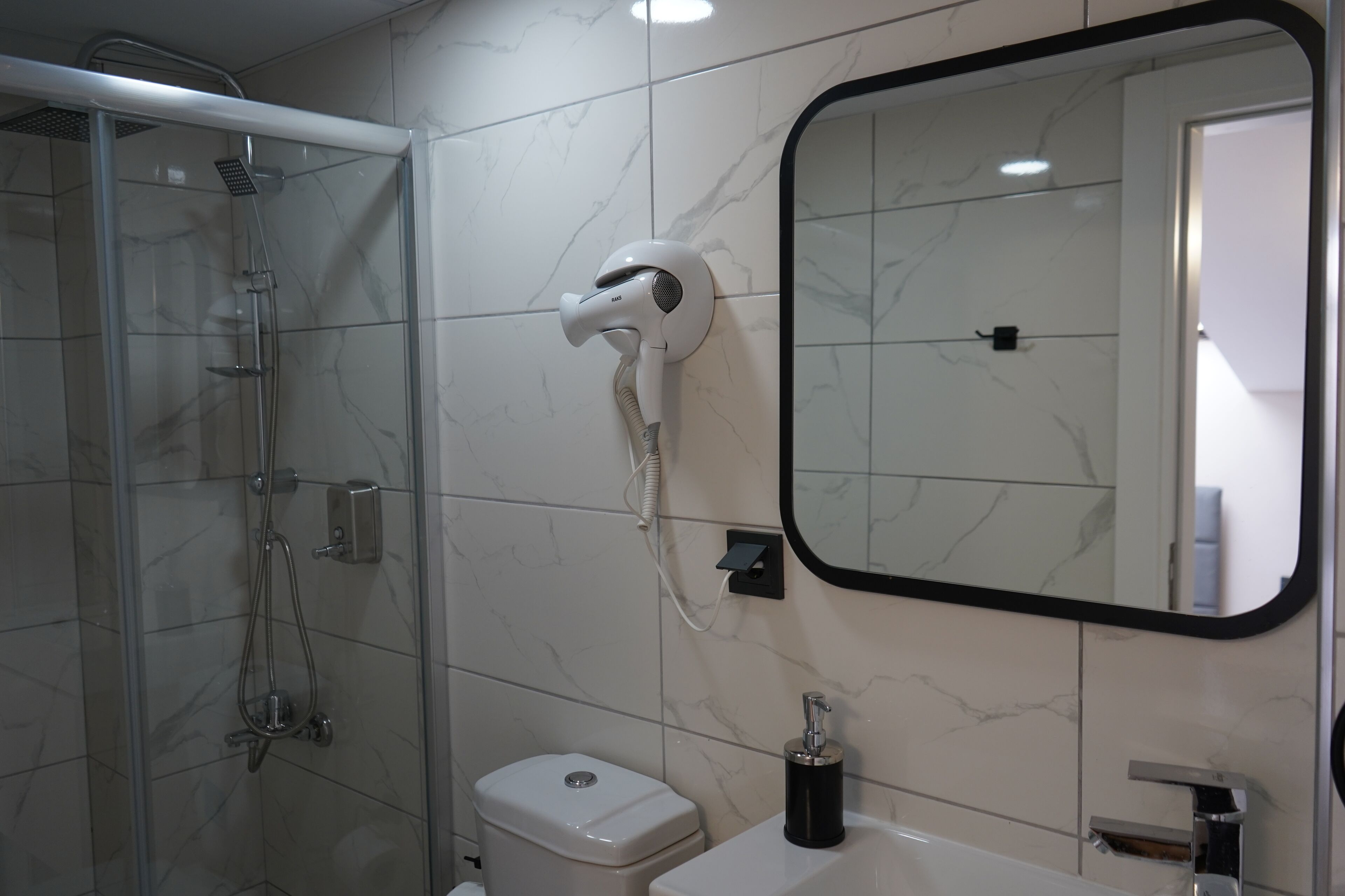 Un baño con ducha de vidrio, inodoro, lavabo y secador de pelo montado en la pared.
