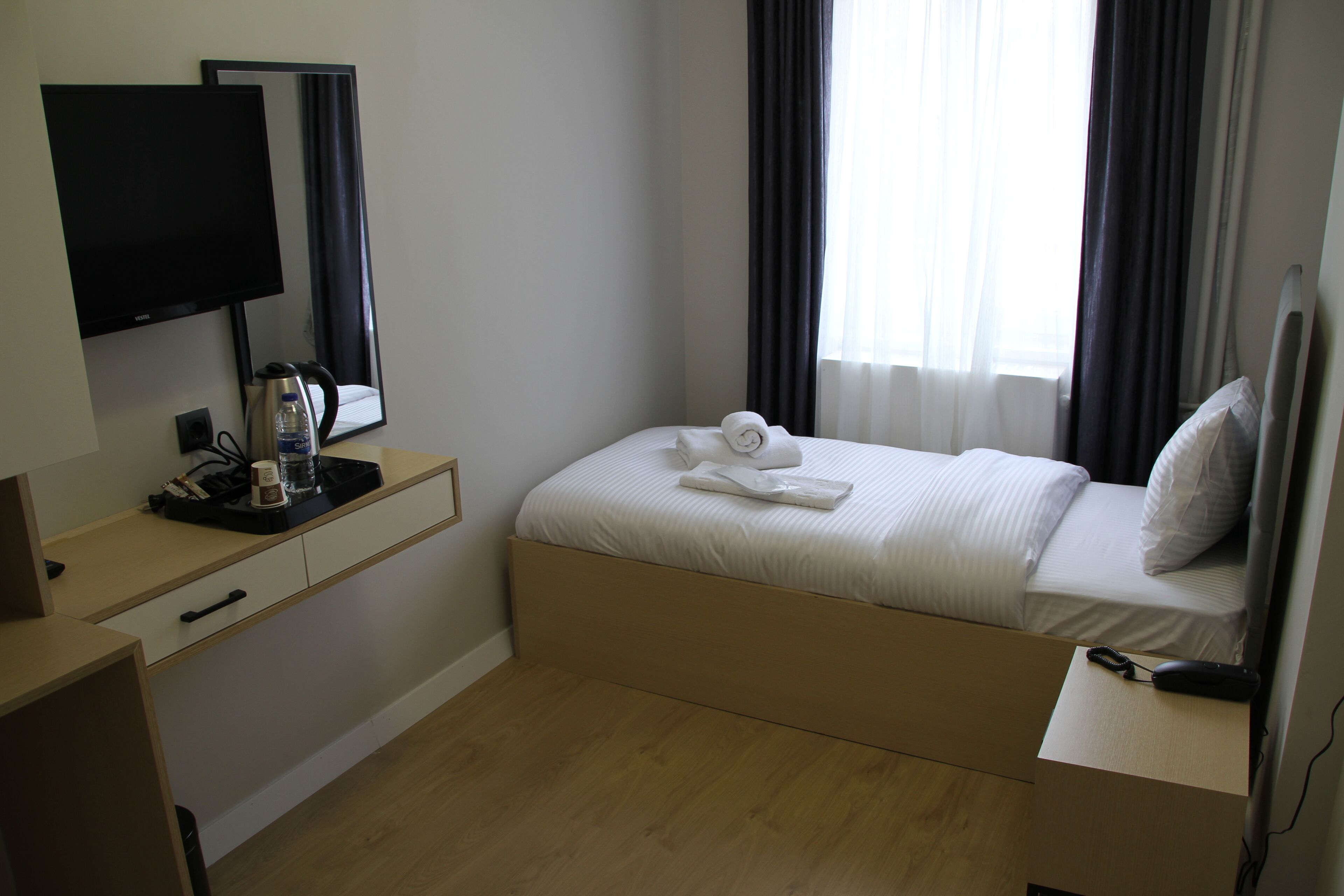 Habitación de hotel con cama, escritorio con televisor de pantalla plana, espejo y ventana con cortinas.
