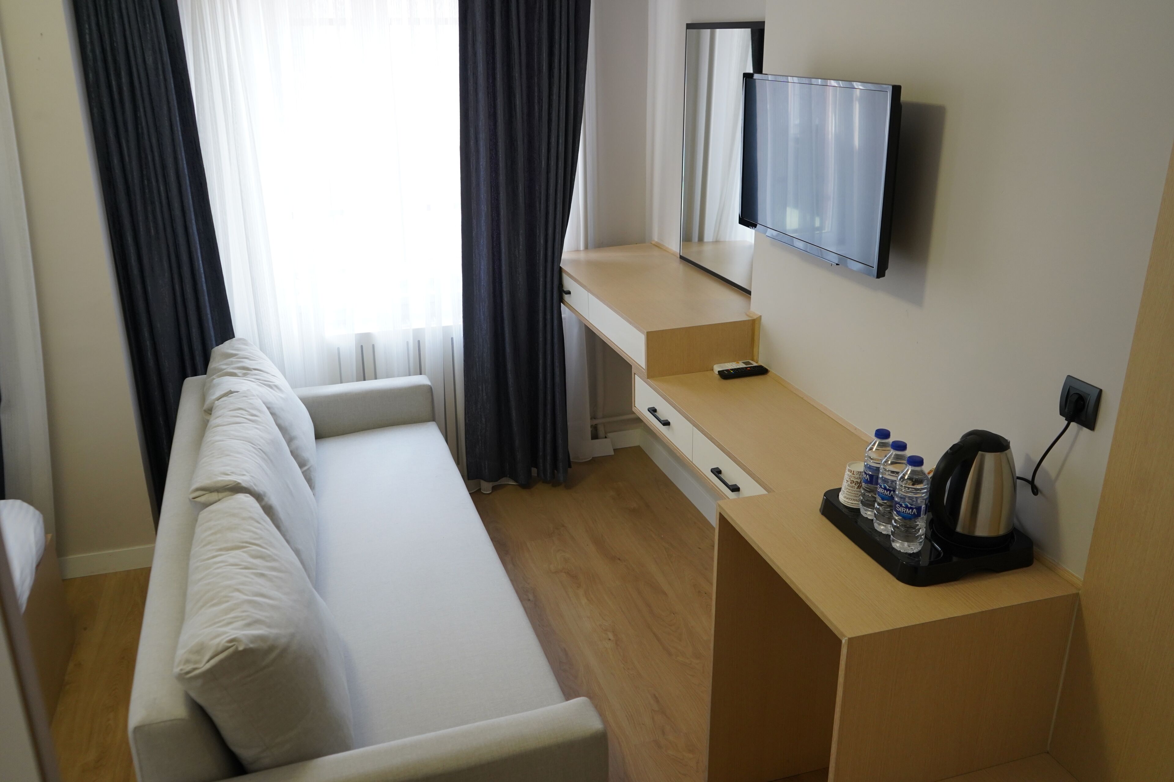 Habitación de hotel pequeña con cama, escritorio con televisión de pantalla plana, cafetera y agua embotellada.