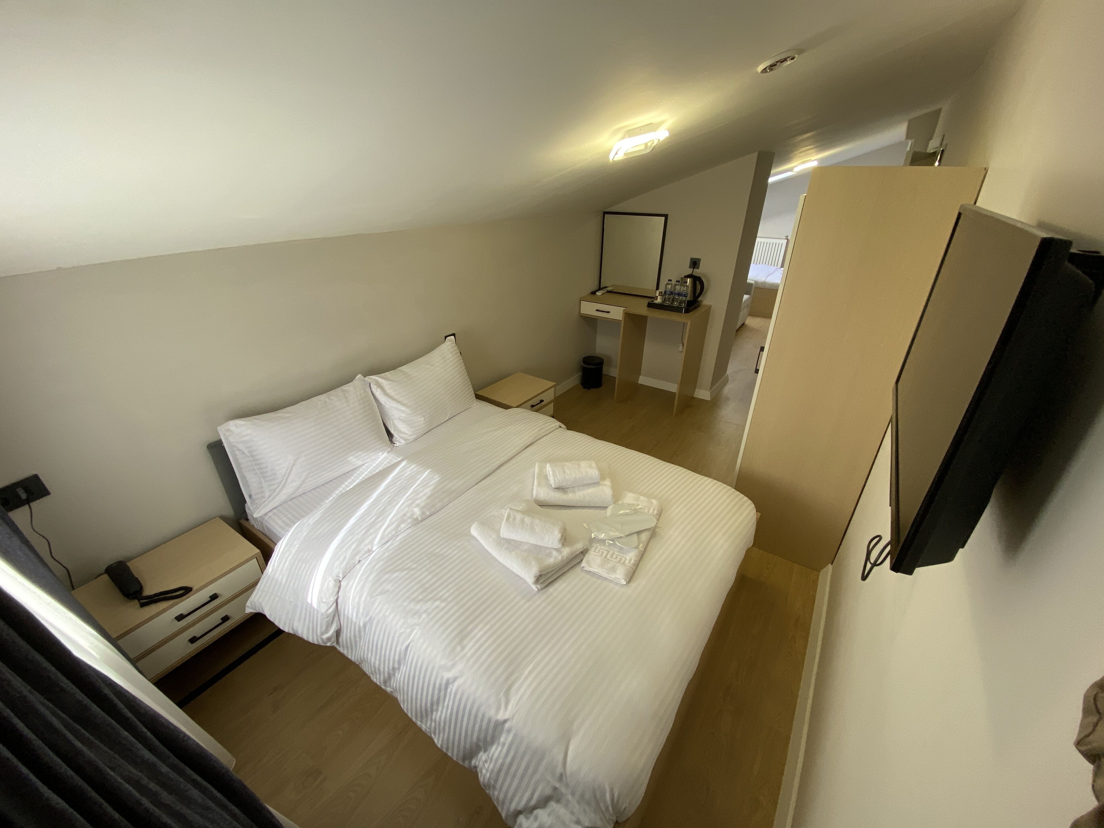 A hotel room with a bed, a bedside table, a desk, a mirror, and a TV.