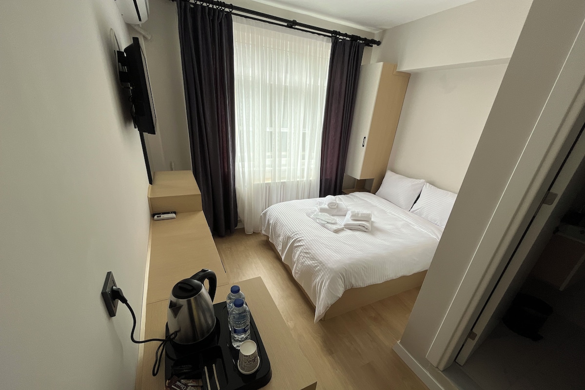 Et hotelværelse med en seng, kaffemaskine, vandflaske og bakke med håndklæder.