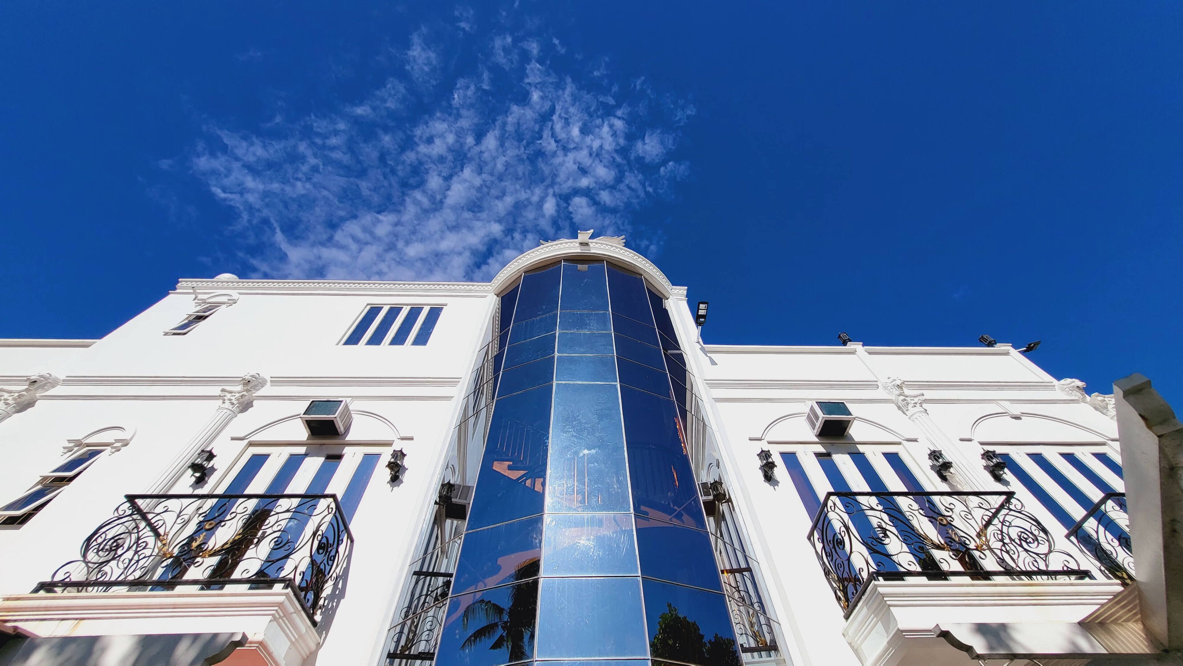 Un edificio con fachada central de vidrio, paredes exteriores blancas y barandillas decorativas de hierro.
