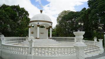 A white gazebo with a dome roof and a cross on top, surrounded by a checkered floor and white balustrades.