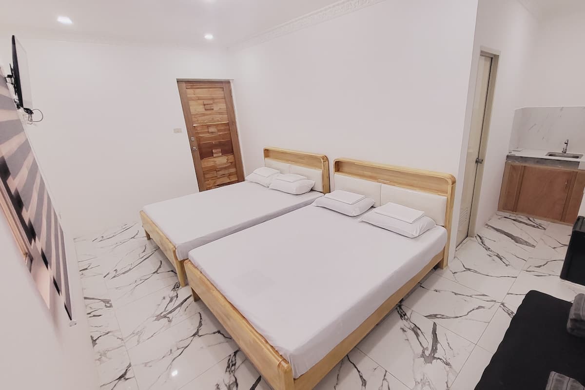 Ein Hotelzimmer mit zwei Betten, einer Holztür, einer kleinen Küchenzeile und einem Marmorboden.