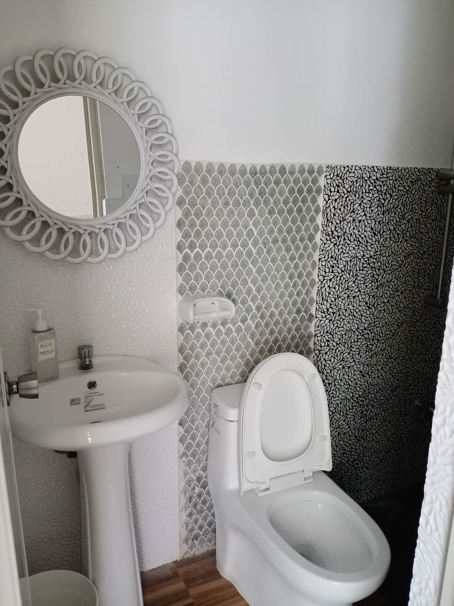 A bathroom with a white sink, a toilet, and a mirror with a circular frame. The walls have a patterned tile design.
