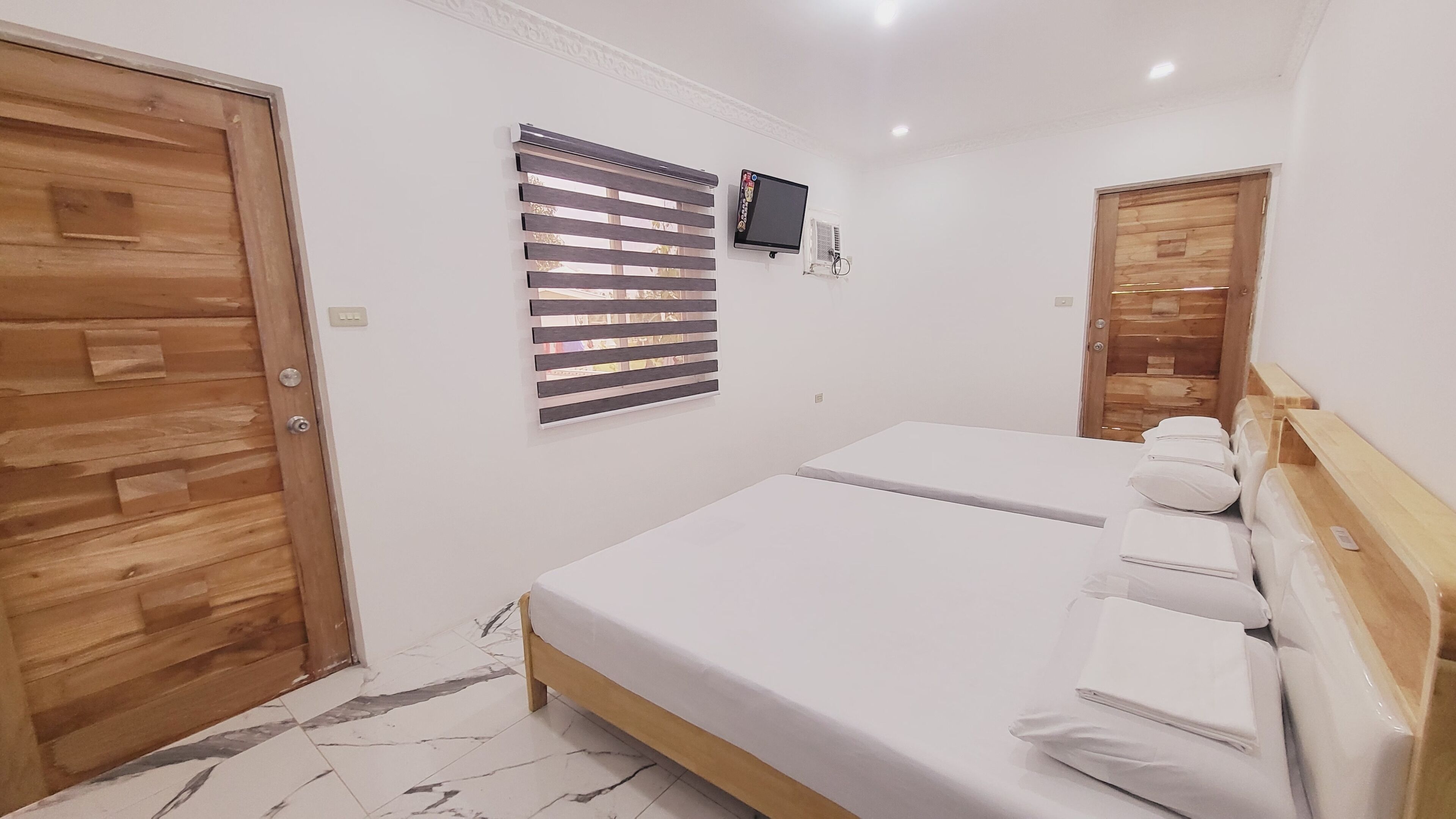 A bedroom with two beds, wooden flooring, a TV, and a window with blinds.