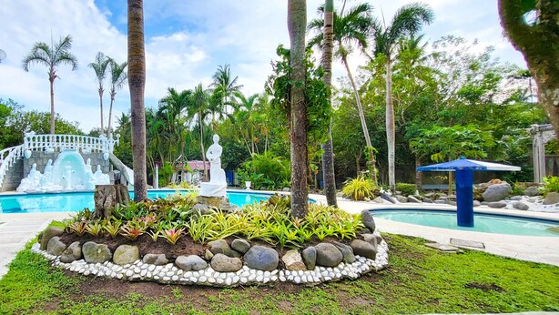A pool area with a fountain, surrounded by palm trees and a decorative fence. - Mancion Bakasyunan Resort San Pablo (San Pablo)