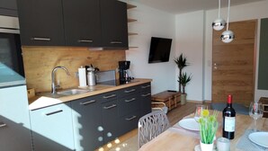 A modern kitchen with dark cabinets, a wooden countertop, and a dining area with a table set for two. - Ferienwohnung 40m² mit Terrasse, bis 3 Personen, Separates Schlafzimmer (Grassau)