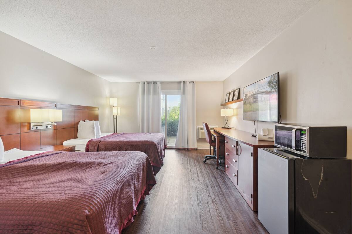 Habitación de hotel con dos camas, un escritorio con computadora, microondas y televisión.