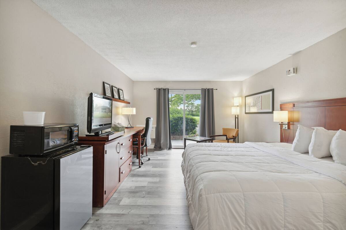Habitación de hotel con cama, escritorio con computadora, televisor, microondas y vista al exterior a través de una puerta corredera.