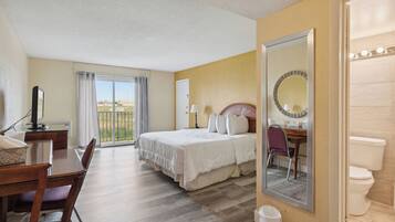 Habitación de hotel con cama, escritorio y silla, baño con inodoro y un espejo grande.