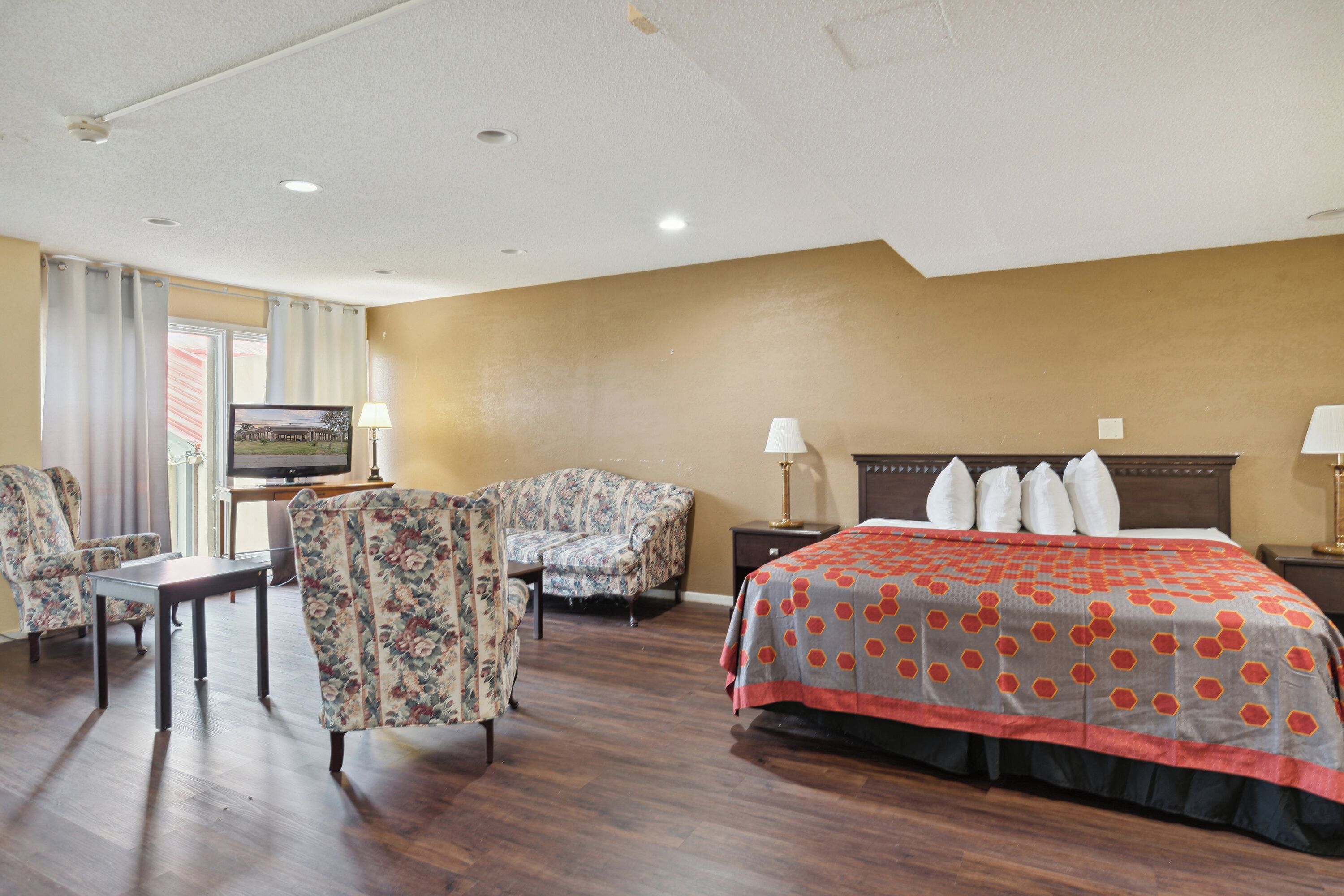 A hotel room with a bed, two chairs, a desk, and a television.